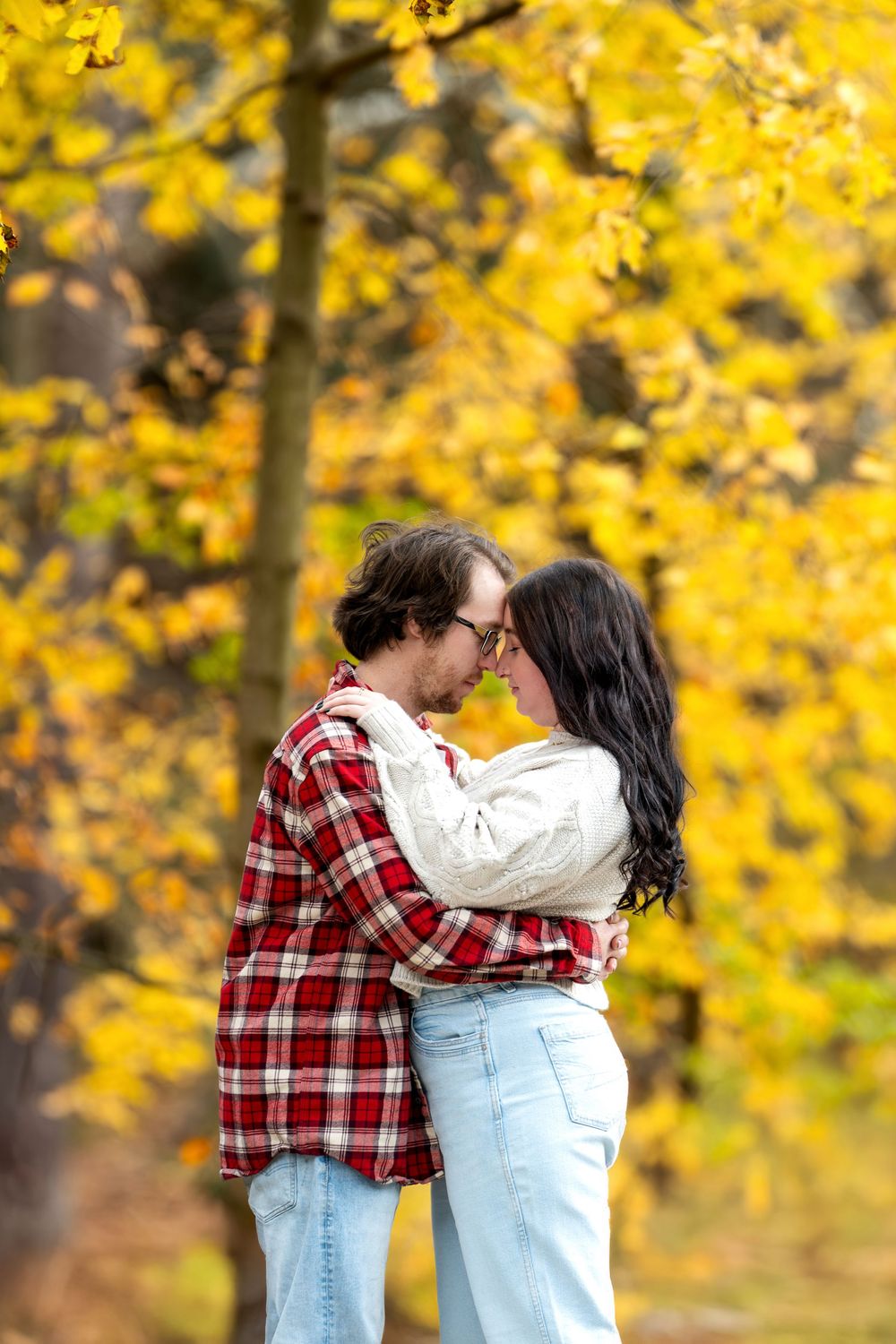 Romantic couple touching foreheads while embracing outdoors in a fall forest setting.