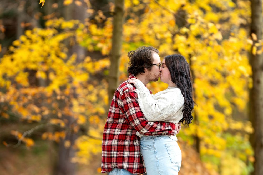 Couple sharing a kiss surrounded by vivid yellow autumn foliage in a park.