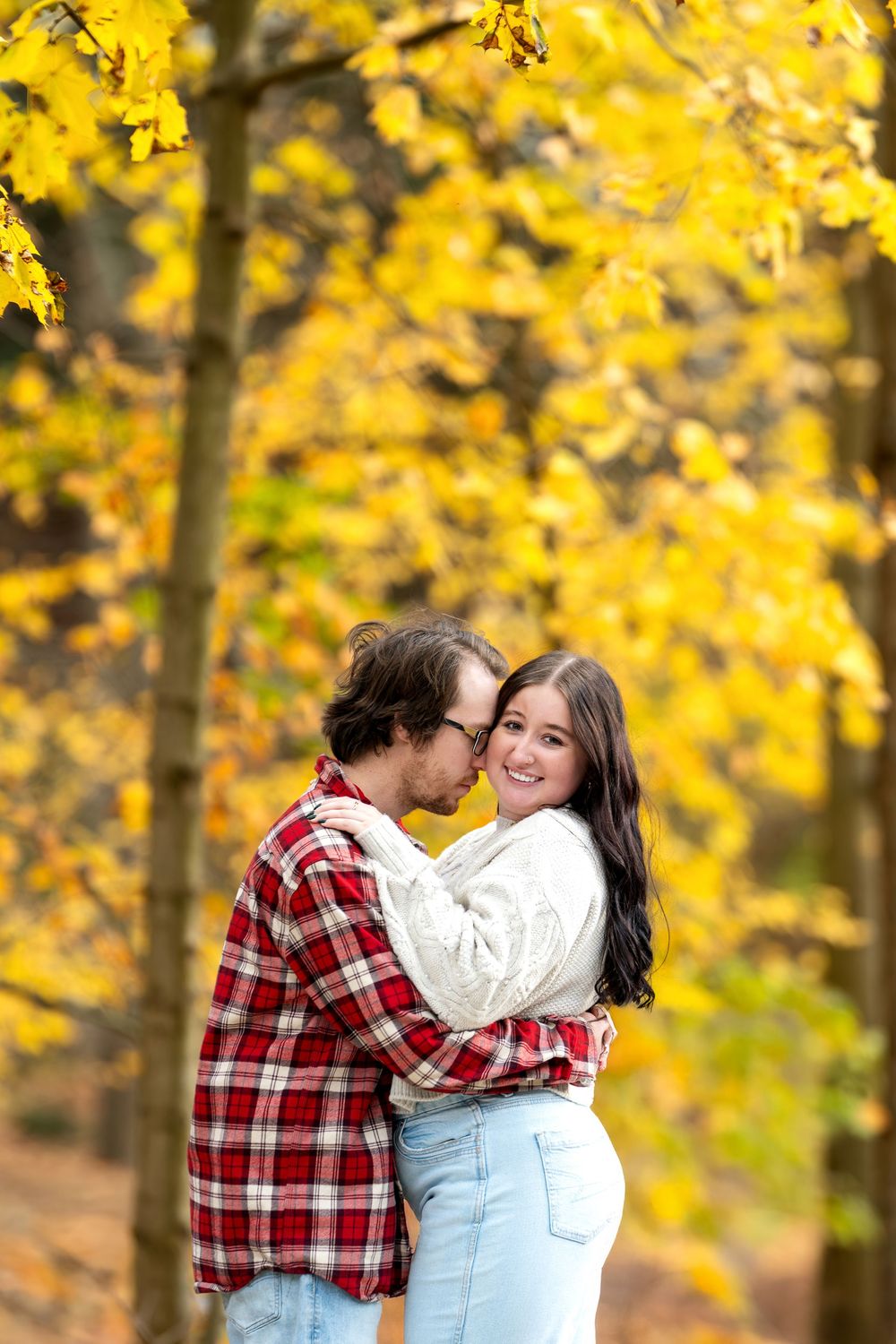 Man kissing woman on the cheek as she smiles in a golden autumn forest.