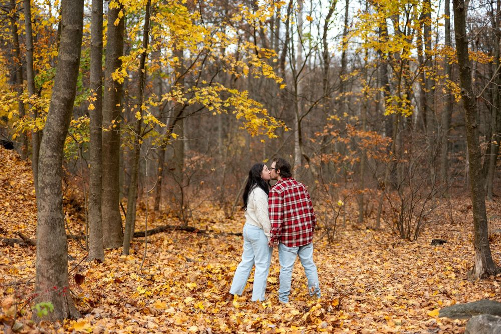 Couple sharing a kiss surrounded by golden autumn foliage in a scenic forest.
