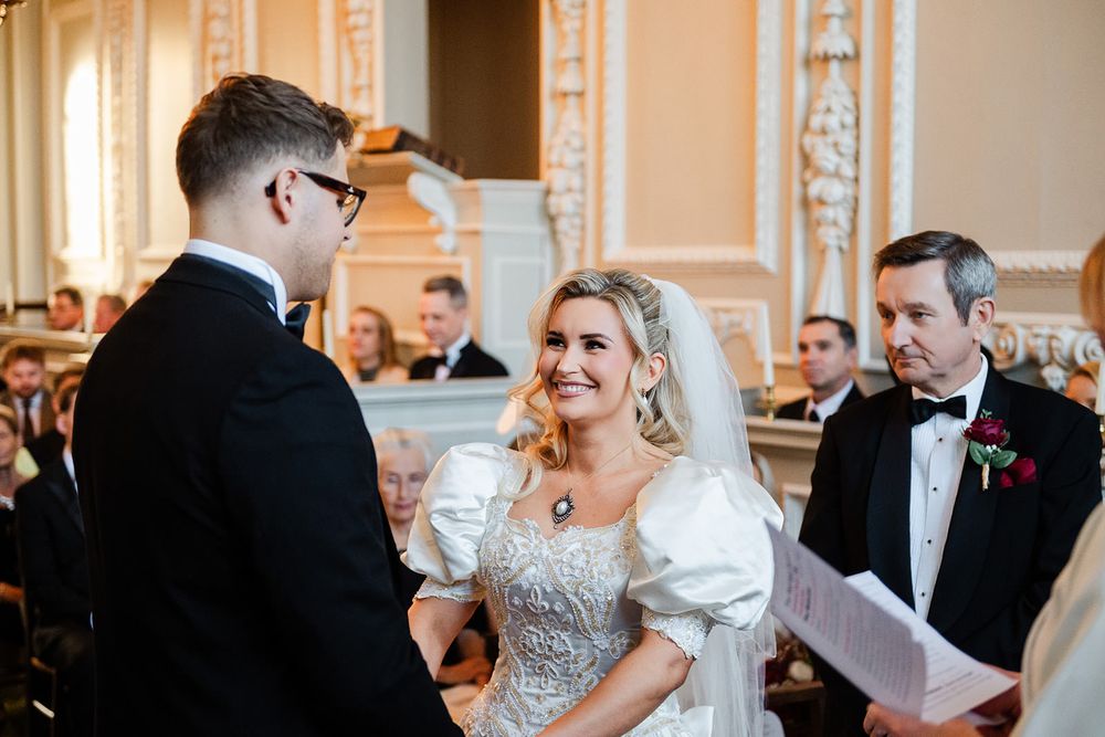 A joyful wedding ceremony takes place in an elegant room with ornate walls and classical decor.