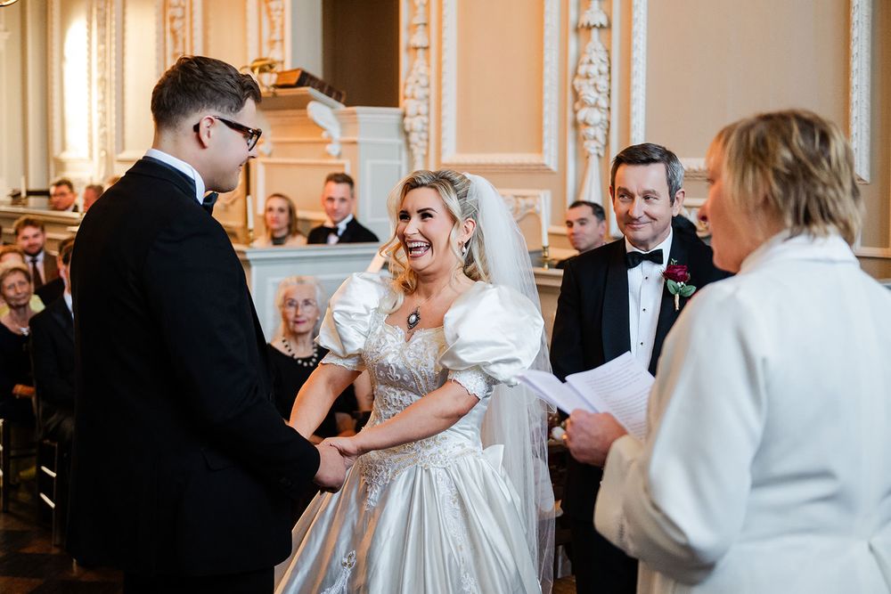 Wedding guests dance and celebrate during an elegant reception in an ornate ballroom with cream-colored walls.