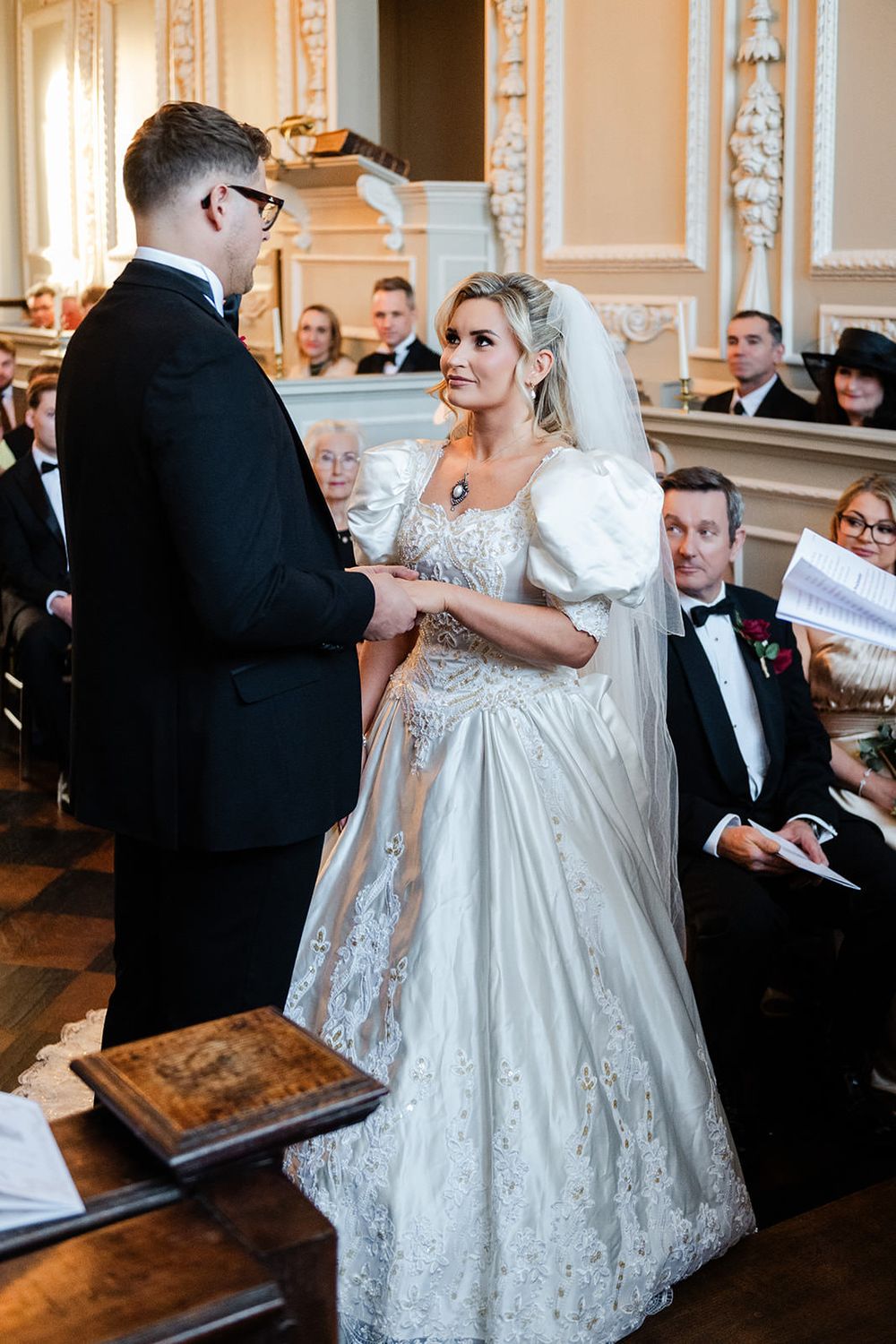 A couple shares a joyful dance moment at their elegant wedding reception in a grand ballroom with ornate decor.