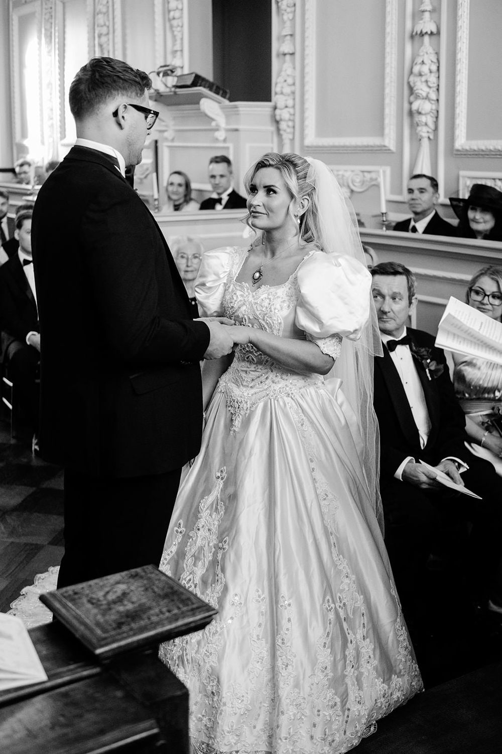 A bride in an elegant white ball gown dances with guests at an ornate ballroom reception.
