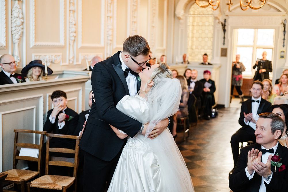 A couple shares their first dance in an elegant ballroom with ornate white walls and decorative moldings.