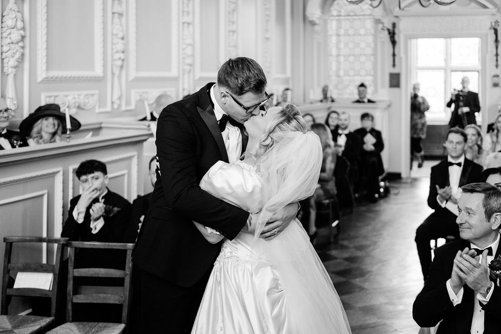 A couple shares their first dance in an elegant ballroom with ornate white walls and decorative moldings.