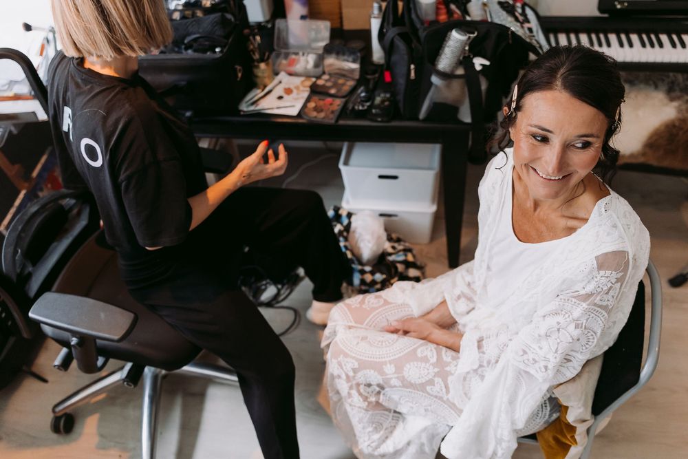 Wedding preparations showing a bride getting her hair and makeup done while surrounded by bridesmaids and stylists.