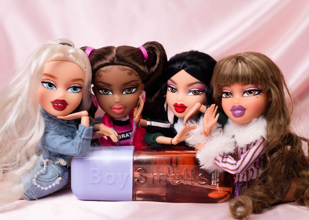Four Bratz dolls with bold makeup posing together against a pink background.