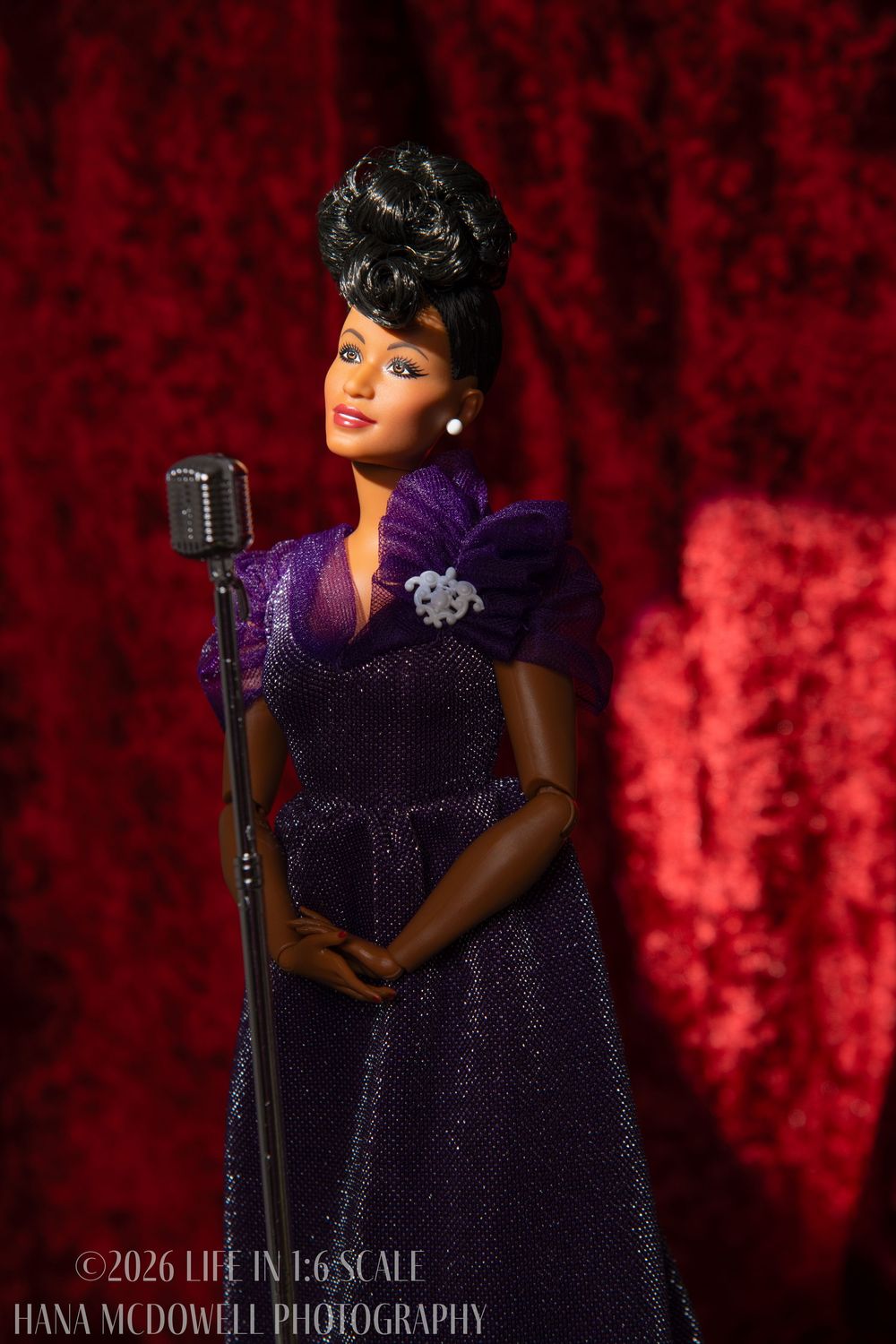 Barbie doll in purple gown standing at a vintage microphone against a rich red velvet background.