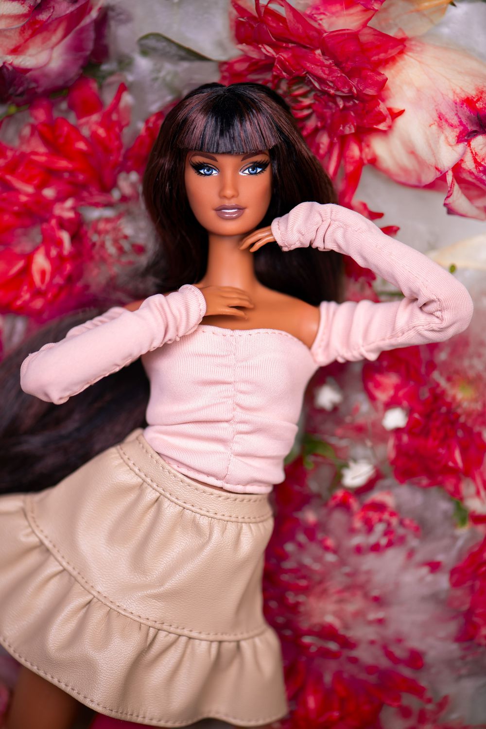 Brunette Barbie doll in pink top and beige skirt posing against a vibrant floral background.