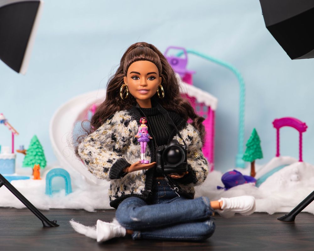 Barbie photographer doll holding a miniature Barbie figure in a winter-themed photography studio.