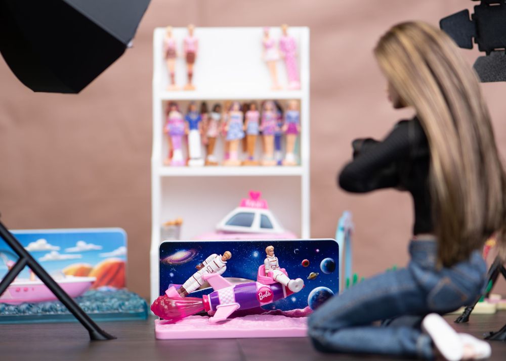 Close-up of a Barbie doll photography studio setup with space-themed backdrop and toy display shelf.