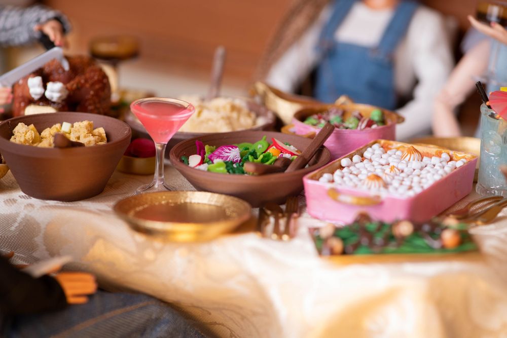Miniature Barbie-scale feast table with colorful dishes, salads, and pink cocktail spread.