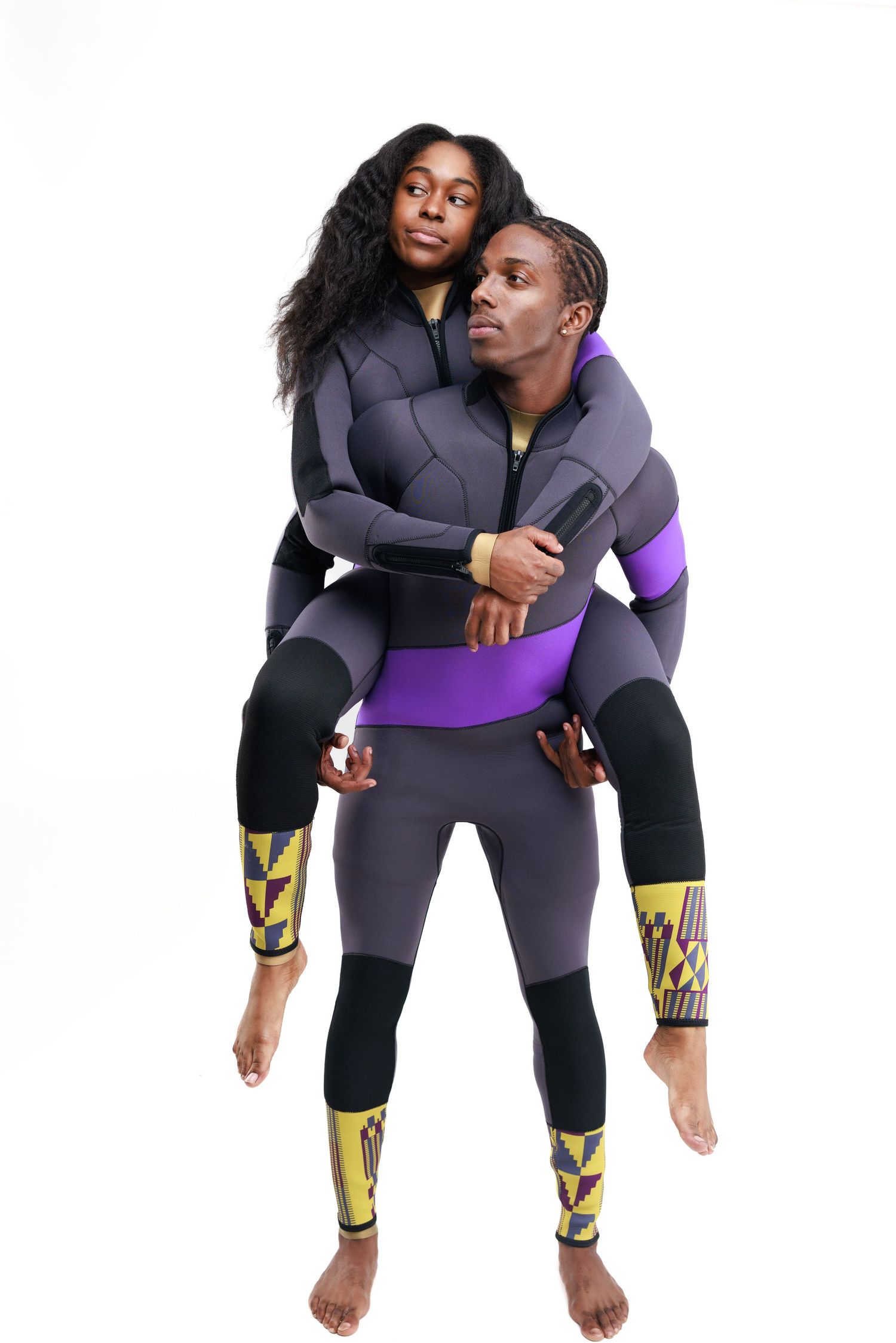 Athletic duo performs playful piggyback poses in matching grey and purple workout attire against white background.