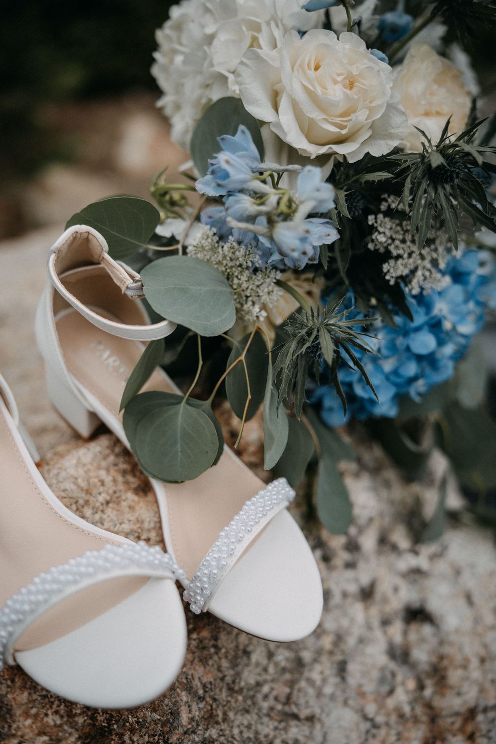 White bridal shoes with delicate floral bouquet featuring cream roses, blue hydrangeas and eucalyptus leaves.