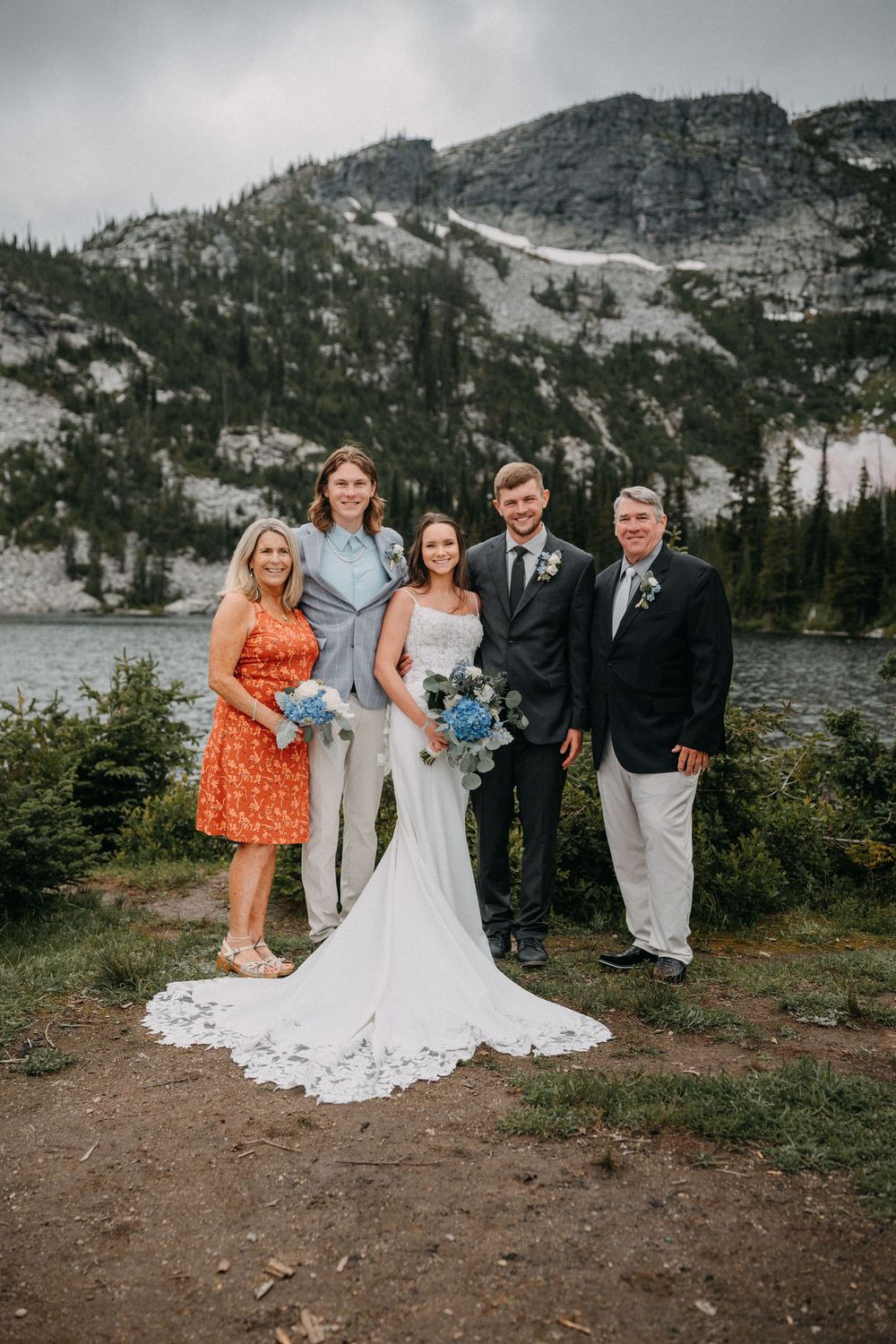 Wedding party poses for group photos in front of a scenic mountain lake backdrop.