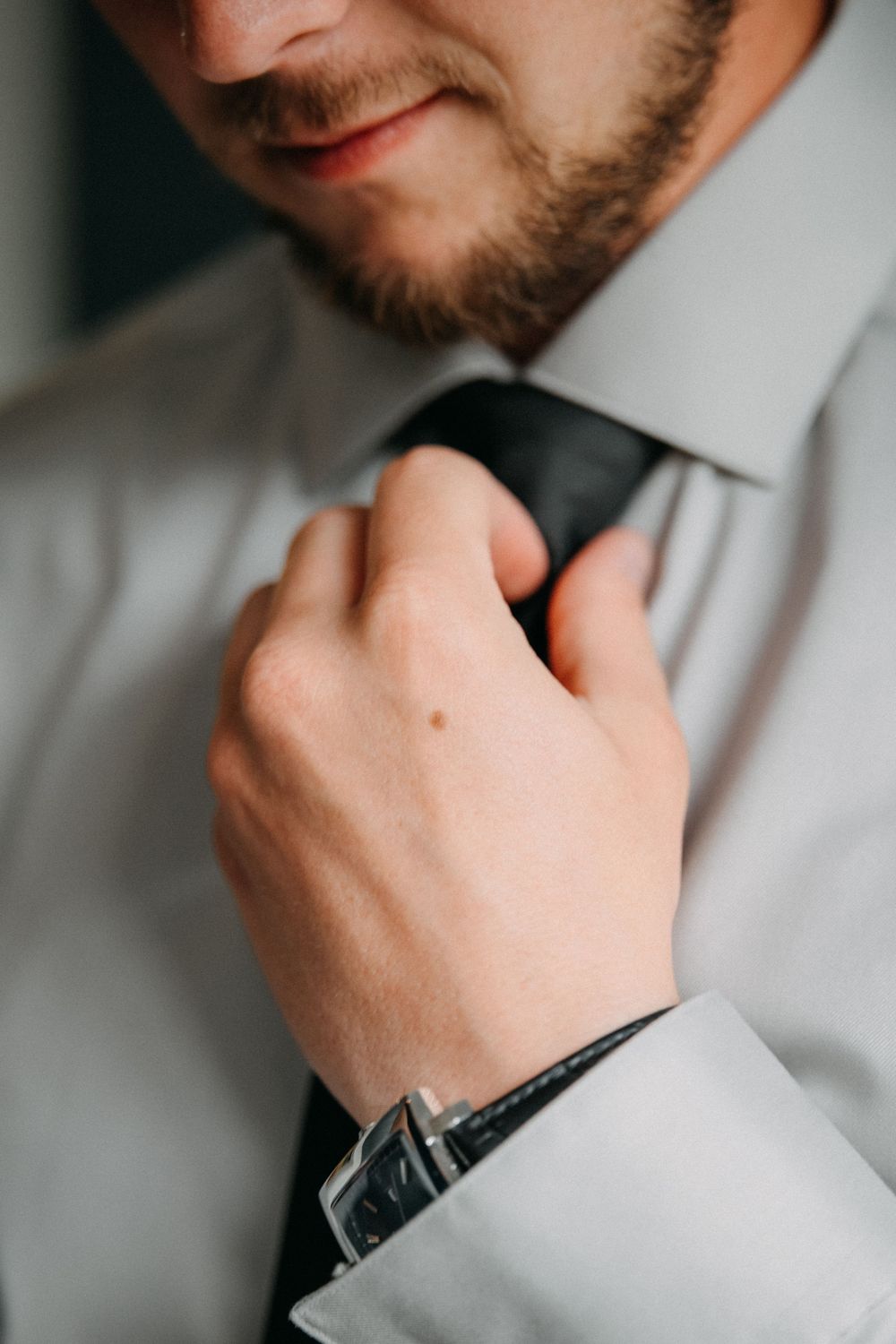 Close-up view of someone adjusting a black tie while wearing a crisp white dress shirt.
