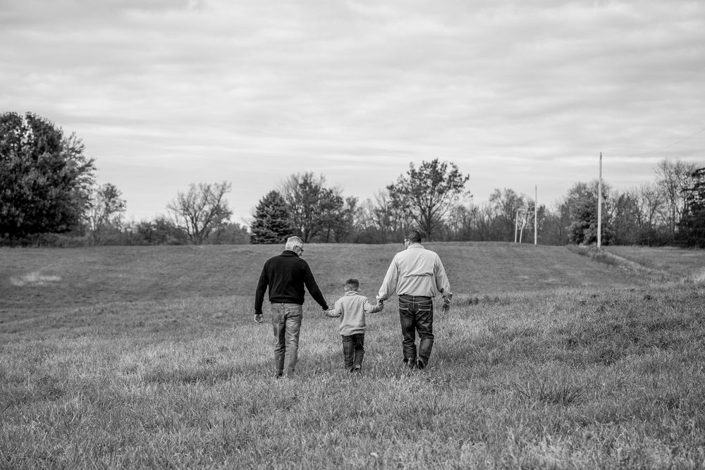 Black and white panoramic sequence showing silhouettes walking through a grassy meadow at dusk.