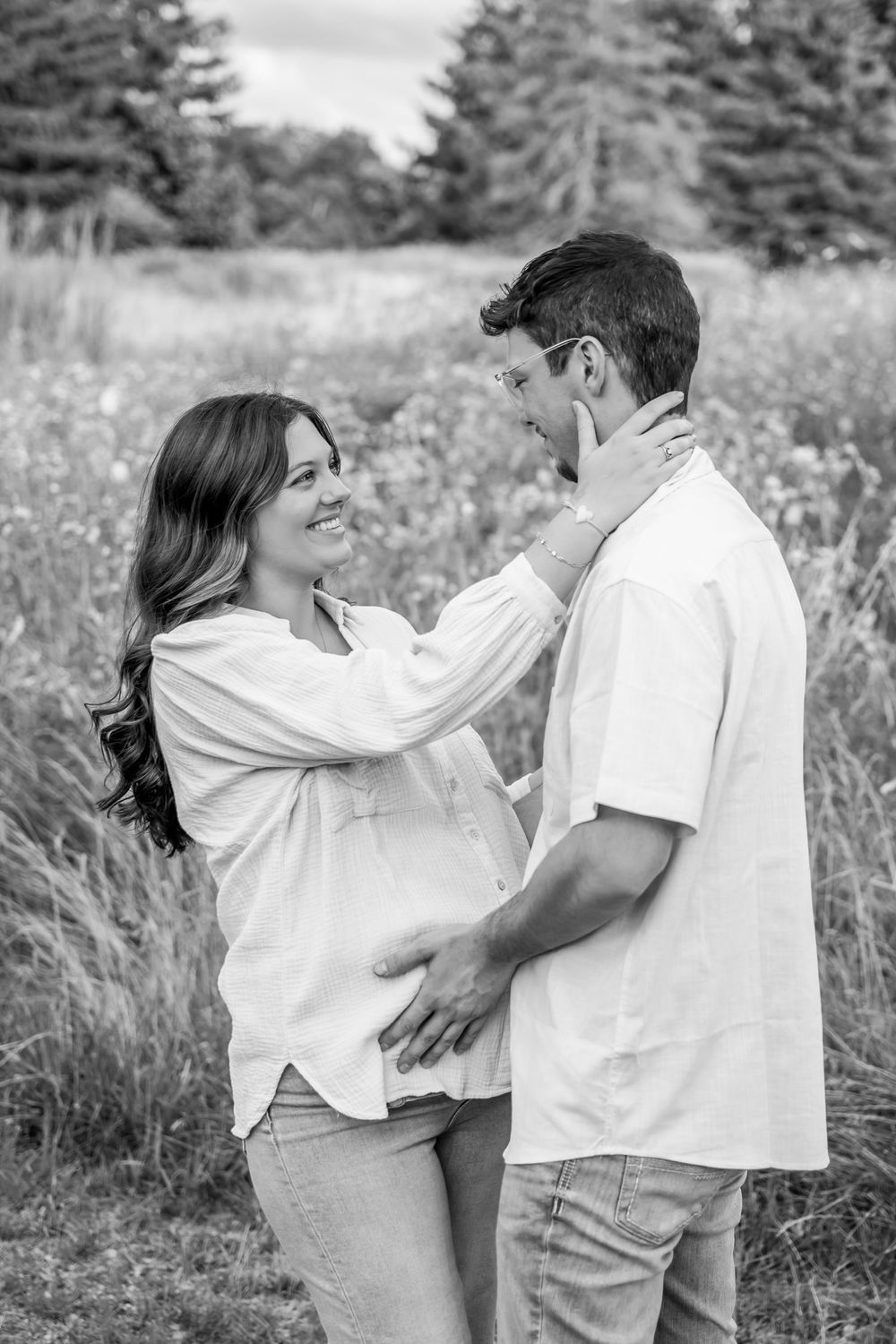 A couple in white outfits share playful and romantic moments together in a grassy field on a summer day.
