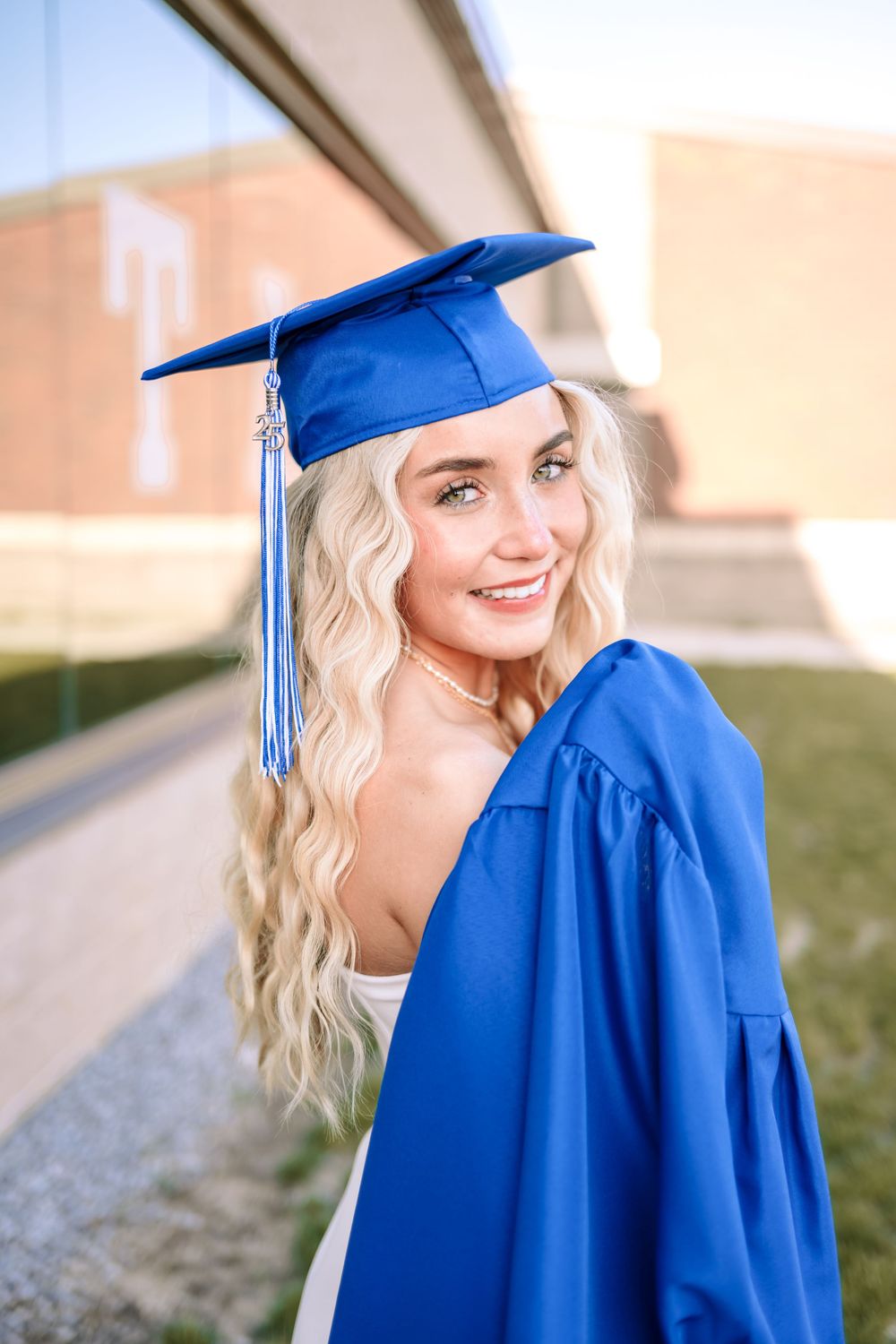 Graduate in bright blue cap and gown smiles during outdoor graduation photo session on sunny day.