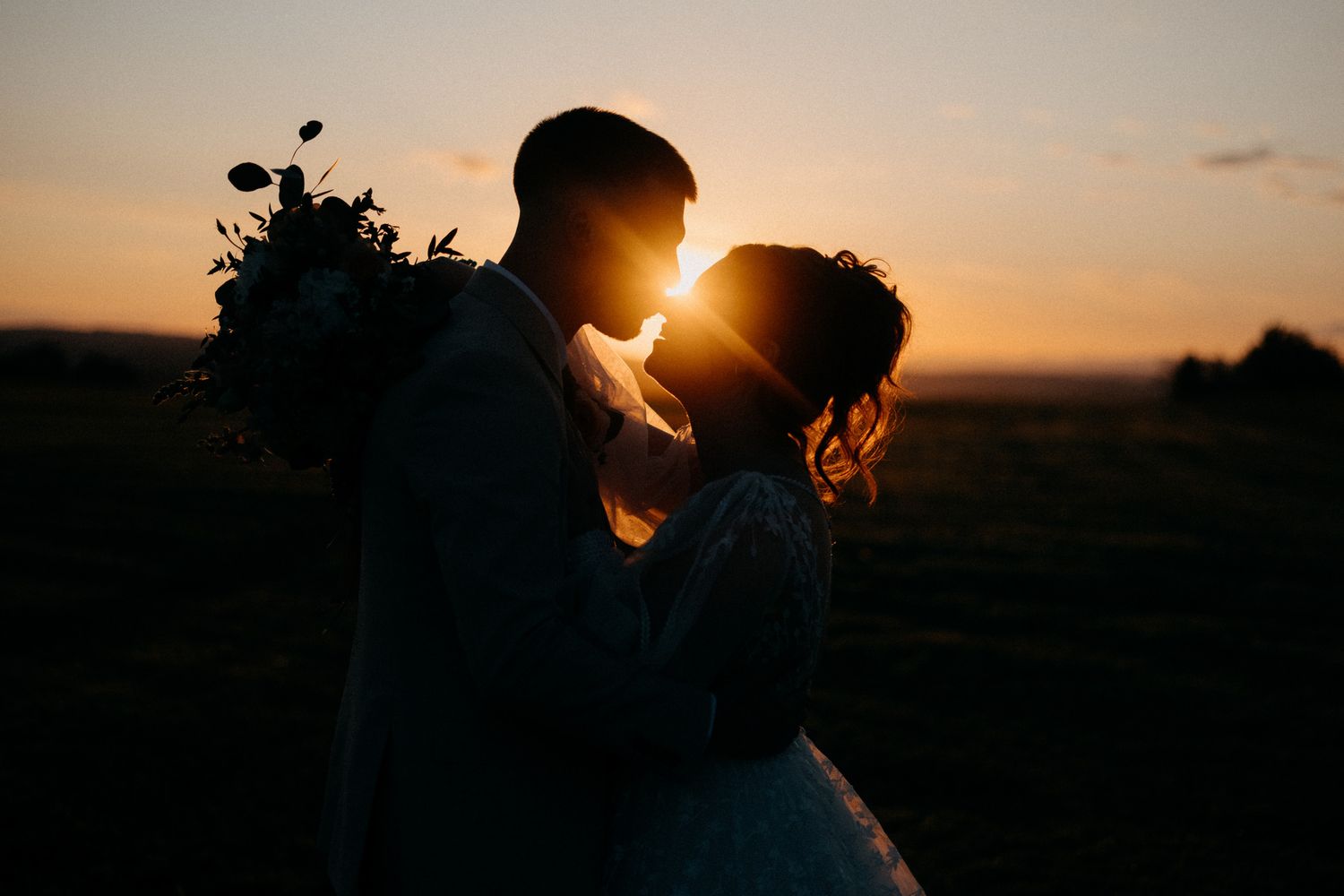 Silhouetted couple embracing in a romantic sunset with golden light glowing behind them.