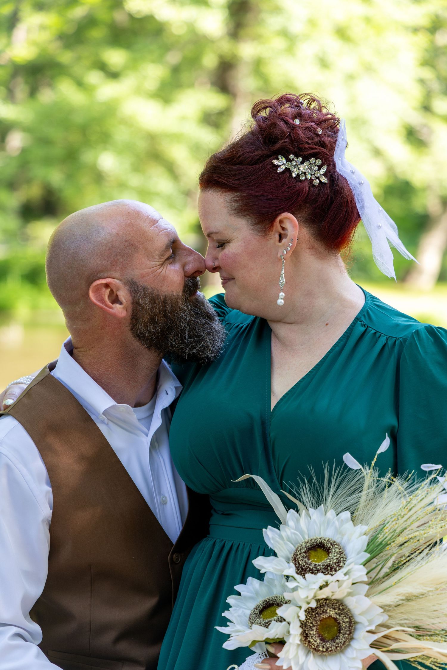 A romantic wedding couple in emerald green and brown share tender moments with sunflowers and wheat in their bouquet.