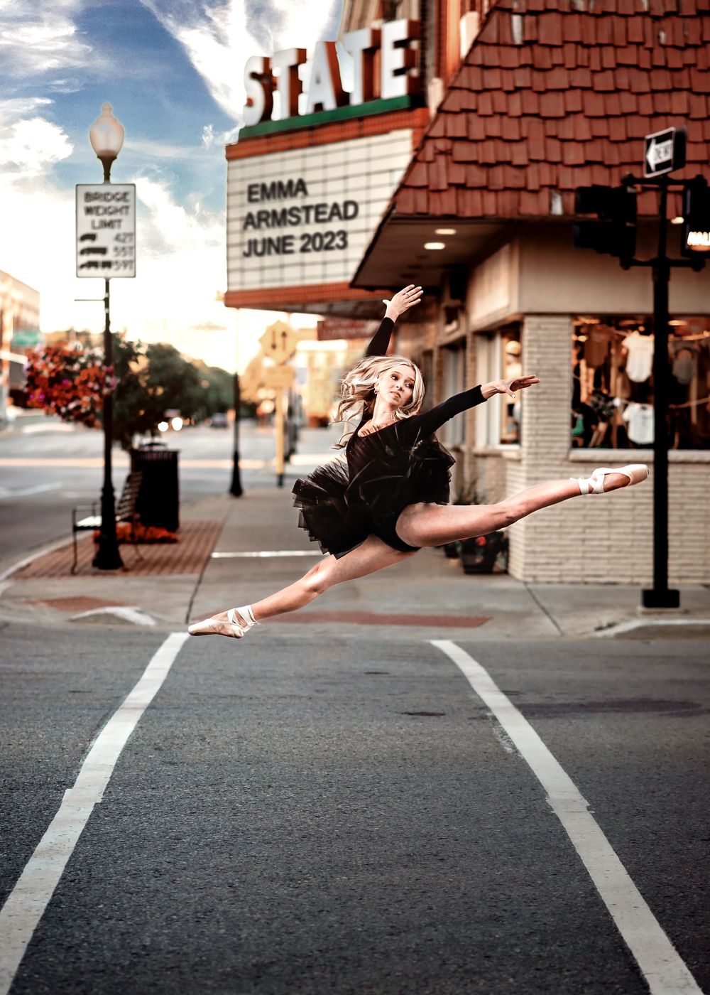 A dancer in a black tutu performs a graceful leap in front of a vintage State Theater marquee on a city street.