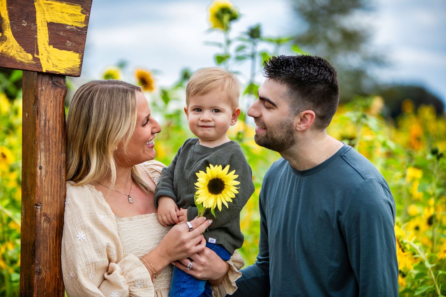 A couple and their small child share a joyful moment together in a vibrant field of blooming sunflowers.