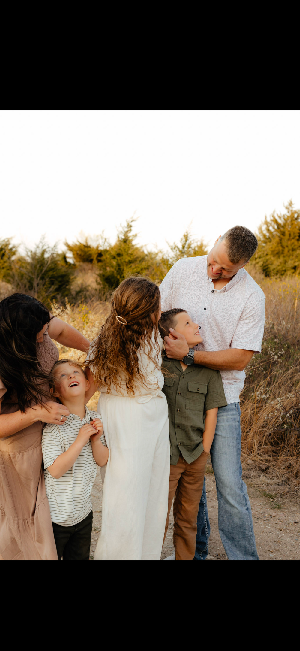 A family shares joyful candid moments together during an outdoor photoshoot at sunset.
