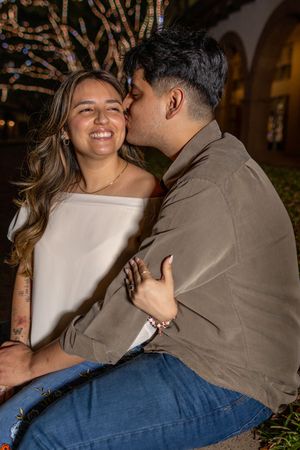 Joyful couple sharing laughter and embraces during an evening photoshoot with fairy lights.