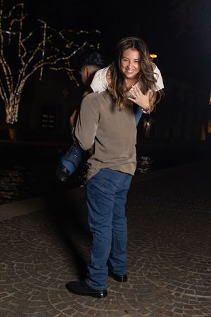 A person in a brown sweater and blue jeans dances and spins on a stone patio at night.