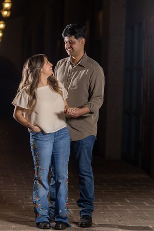 A couple dances together on a brick patio at night with decorative lights in the background.