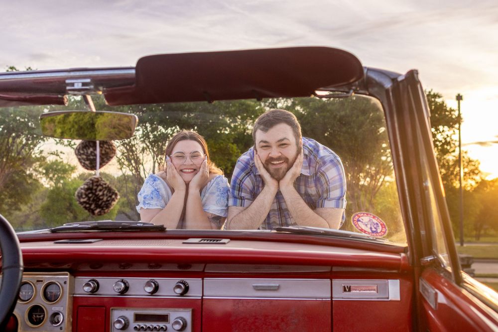 Smiling couple leaning on red convertible car at sunset, enjoying a casual outdoor moment together.