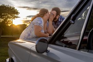 Couple sharing a romantic moment leaning on a vintage car hood at golden sunset in a park.