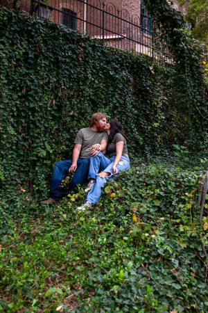 A couple relaxing against an ivy-covered wall in an urban setting.