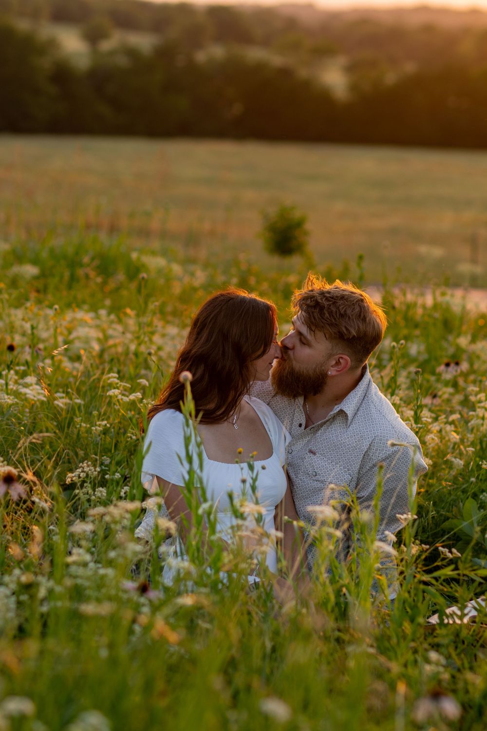 Couple shares intimate moment lying in meadow of wildflowers at dusk.