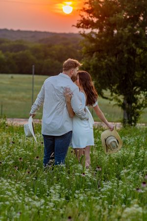 Couple strolling through flowering meadow during dramatic orange sunset.