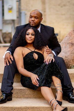 Romantic couple poses intimately on stone steps in elegant evening wear during outdoor photo session.
