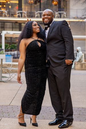 Couple shares playful moments during engagement photoshoot wearing formal black attire outdoors.