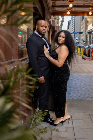 A couple in formal attire shares a romantic moment during a photo session on a city sidewalk.