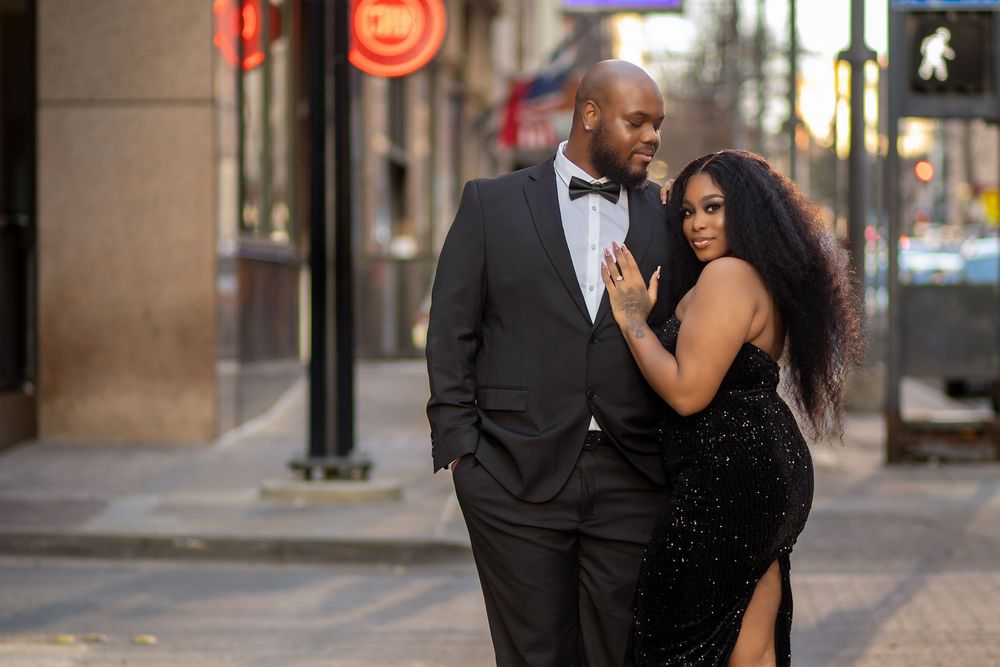 A couple in formal attire shares an intimate moment on a city sidewalk during an urban engagement photoshoot.