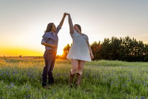 Two people dancing and holding hands in a flower-filled meadow at sunset.