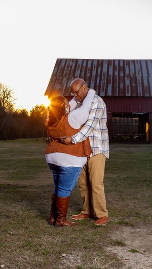 A romantic sunset engagement photo session with a couple embracing in front of a rustic barn.