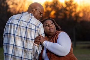 A romantic couple embraces during golden hour sunset in a park setting with warm autumn colors in the background.