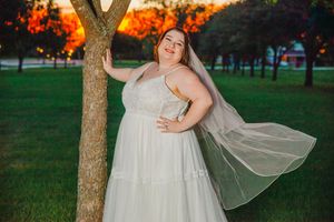 A bride in a flowing dress poses gracefully against trees during golden hour.