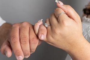Close-up of two hands holding, one wearing a diamond engagement ring and a silver band on their wedding finger.