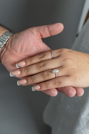 Close-up of two hands touching, woman wearing a diamond engagement ring with French tip nails and a silver watch on mans wrist.