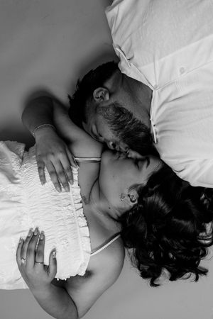 Black and white photo of a couple sharing a tender kiss while lying in bed together.