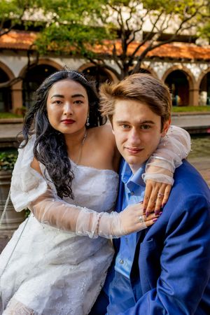 A couple in wedding attire share intimate moments outdoors with the bride in white lace and groom in blue suit.