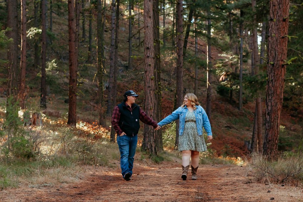 Two people walk hand in hand along a scenic forest trail lined with tall pine trees during autumn.